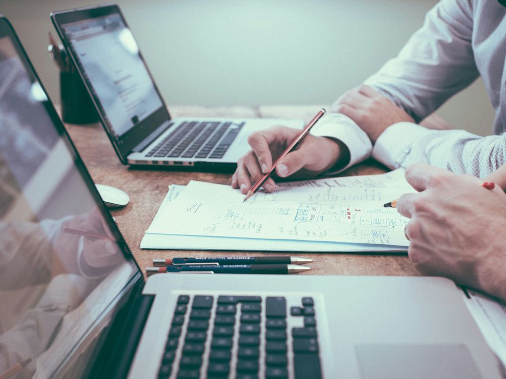 Two people reviewing financial figures and diagrams on paper beside laptops